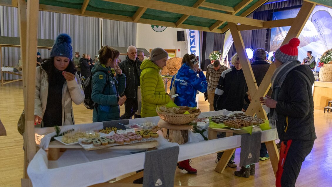 Ein festlicher Stand mit verschiedenen Snacks und Leckereien. Menschen stehen zusammen und genießen die Atmosphäre. | © Michael Simonlehner