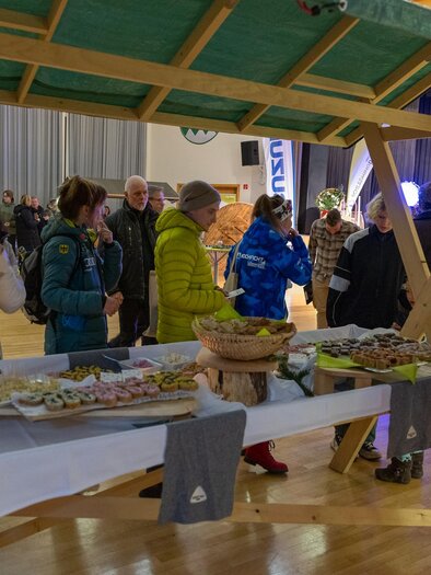 A festive stand with various snacks and treats. People are gathered together and enjoying the atmosphere. | © Michael Simonlehner