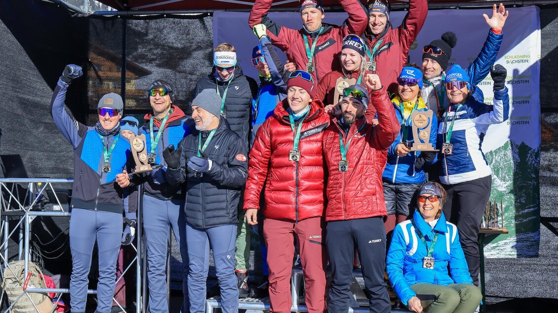 Eine Gruppe von Menschen steht auf dem Siegertreppchen und feiert mit Medaillen. Die Atmosphäre ist festlich und sportlich, im Hintergrund ist eine Zeltkonstruktion erkennbar. | © Michael Simonlehner