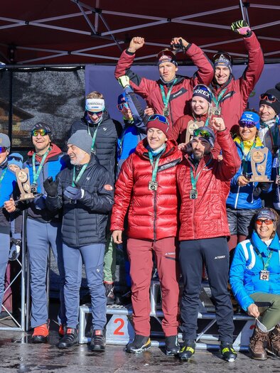 A group of people stands on the winner's podium and celebrates with medals. The atmosphere is festive and sporty, and in the background, a tent structure is visible. | © Michael Simonlehner