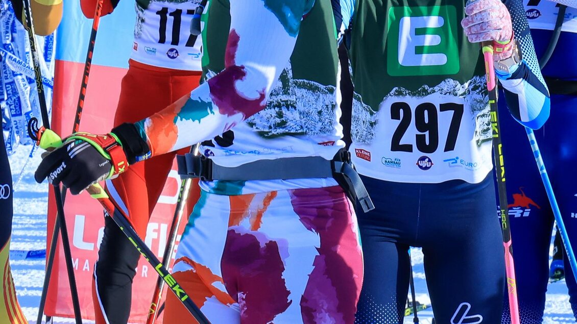 Zwei Skilangläufer stehen auf einer schneebedeckten Strecke und unterhalten sich. Beide tragen bunte Sportbekleidung und Skiausrüstung. | © Michael Simonlehner