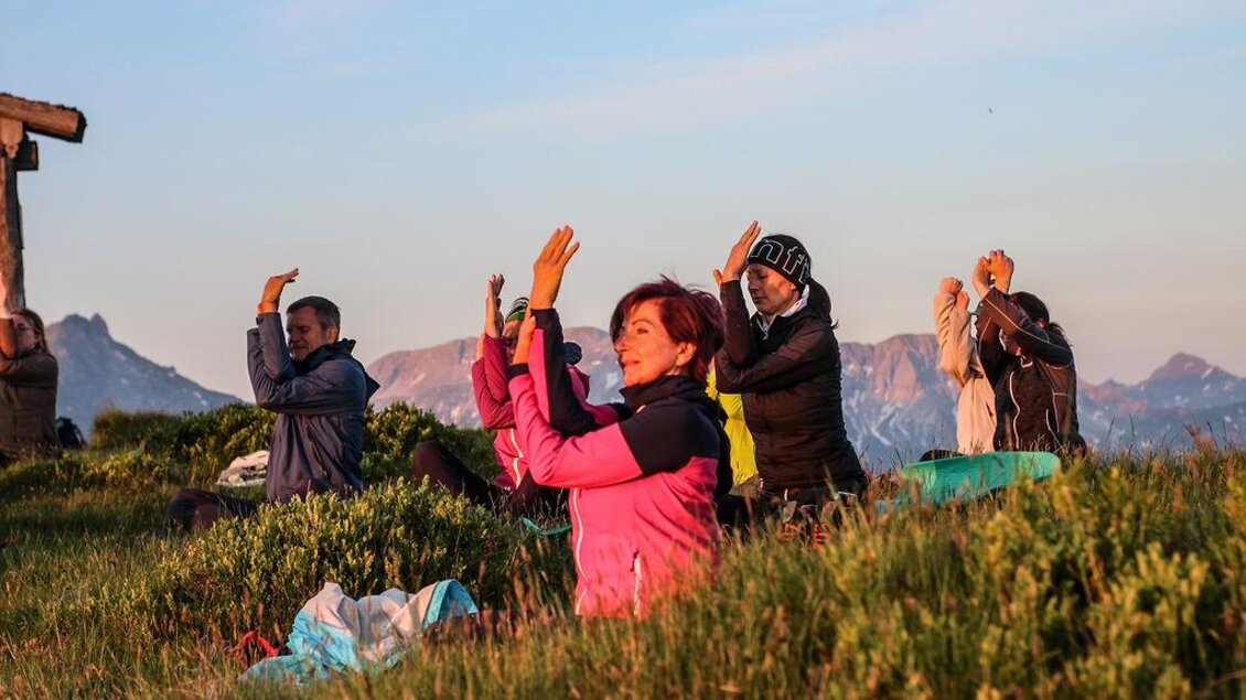 Bei warmem Morgenlicht praktiziert die Gruppe eine ruhige Yoga-Abfolge mitten in der Natur. Die Berge im Hintergrund und die sanfte Sonne schaffen einen kraftvollen Start in den Tag. | © Das Bergyogafestival