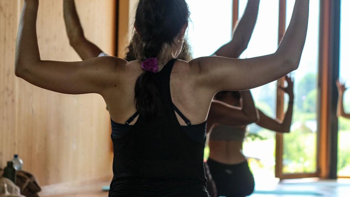 Im lichtdurchfluteten Raum übt die Gruppe eine kraftvolle Yoga-Haltung. Die Holzarchitektur und der Blick ins Freie schaffen ein harmonisches Umfeld. | © Das Bergyogafestival