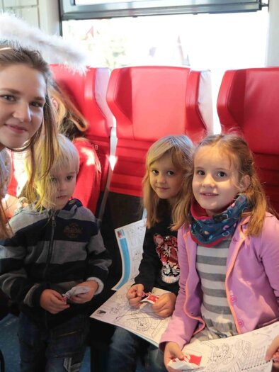 Ein fröhliches Kinderevent in einem Zug. Ein Mädchen im Engelkostüm steht neben drei Kindern, die mit Malutensilien beschäftigt sind. | © Andreas Kügerl