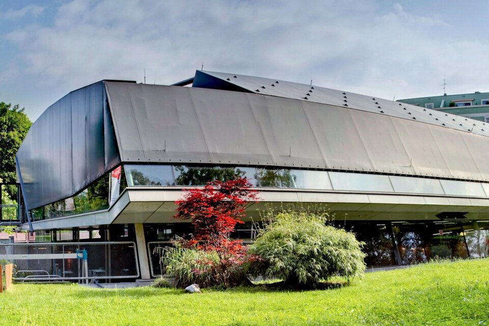 Ein modernes Gebäude mit einer einzigartigen, gewellten Fassade. Umgeben von Grünflächen und Bäumen. | © Frida & Fred_Hannes Loske