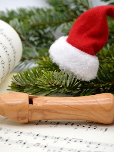 A recorder lies on sheet music, surrounded by pine branches. A red Santa hat adorns the flute and brings a festive atmosphere. | © pixabay