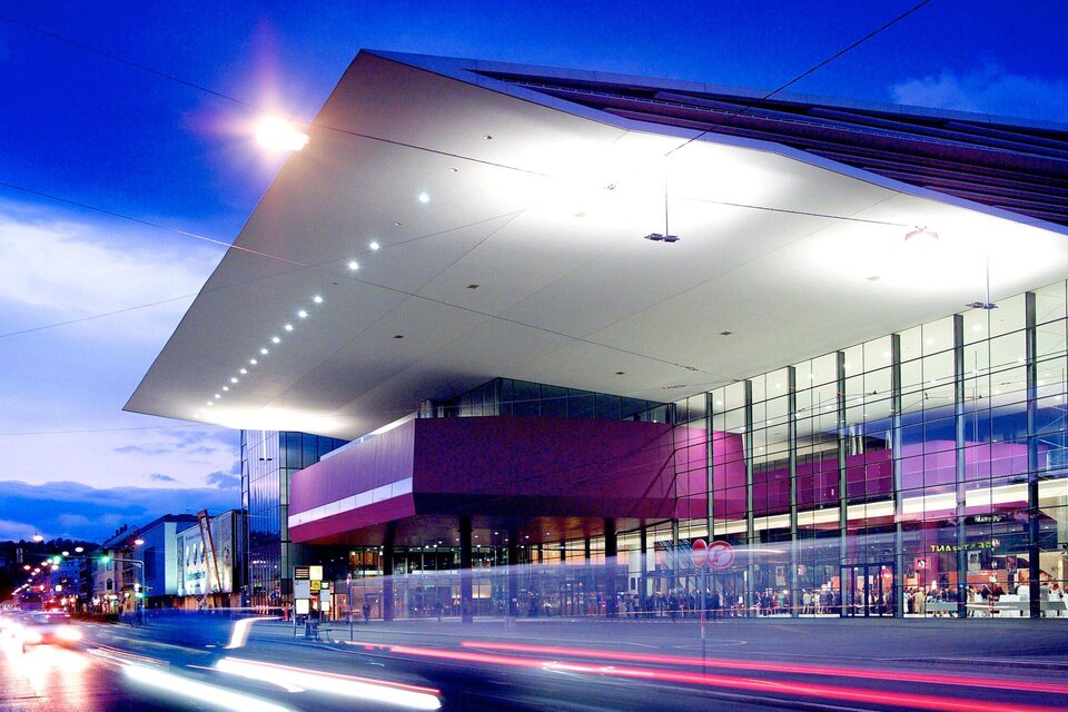 Ein modernes Gebäude mit einer großen Glasfront bei Dämmerung. Das Dach ist markant und gut beleuchtet. | © MCG - Werner Krug