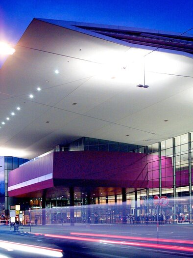 Ein modernes Gebäude mit einer großen Glasfront bei Dämmerung. Das Dach ist markant und gut beleuchtet. | © MCG - Werner Krug