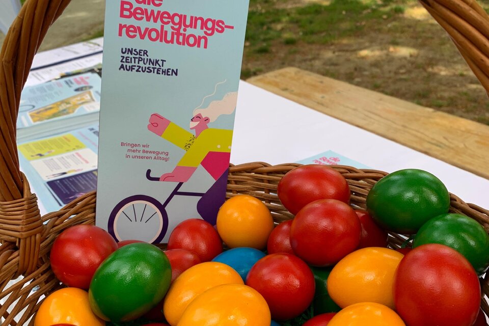 Ein Korb mit bunten Holzspielzeugen in verschiedenen Farben, darunter rote, grüne, gelbe und blaue Kugeln. Neben dem Korb steht ein Flugblatt mit dem Titel „Die Bewegungsvrevolution“. | © Oststeiermark Tourismus