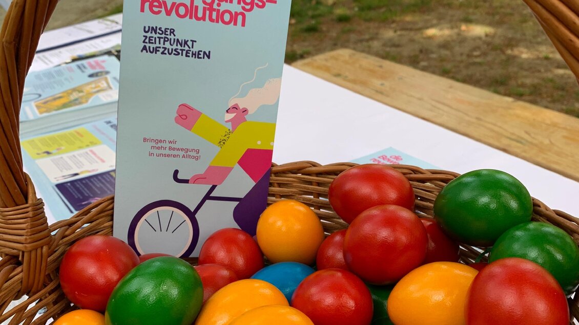 Ein Korb mit bunten Holzspielzeugen in verschiedenen Farben, darunter rote, grüne, gelbe und blaue Kugeln. Neben dem Korb steht ein Flugblatt mit dem Titel „Die Bewegungsvrevolution“. | © Oststeiermark Tourismus