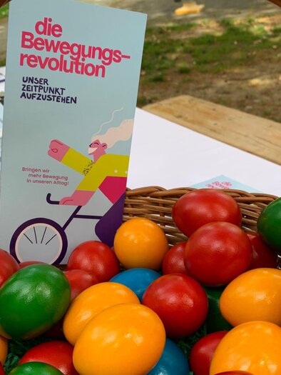 A basket with colorful wooden toys in various colors, including red, green, yellow, and blue balls. Next to the basket is a flyer titled "The Movement Revolution." | © Oststeiermark Tourismus