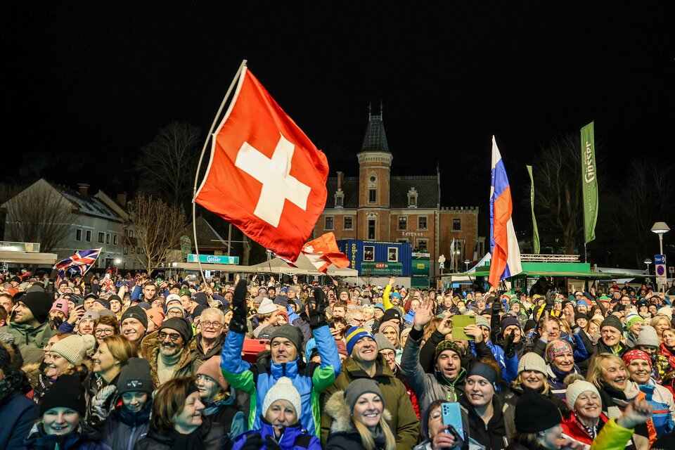 Eine große Menschenmenge feiert bei Nacht und hält eine Schweizer Flagge hoch. Im Hintergrund ist ein beeindruckendes Gebäude zu sehen. | © Martin Huber
