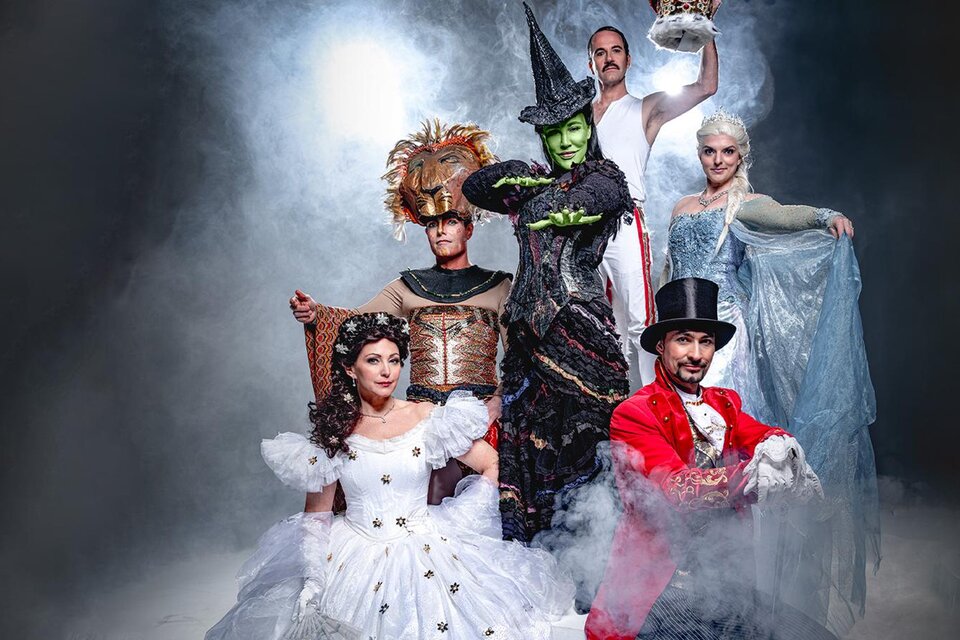 Eine Gruppe von Schauspielern in bunten Kostümen steht auf einer Bühne, umgeben von Nebel. Die Charaktere umfassen eine Hexe, eine Prinzessin und weitere fantasievolle Gestalten. | © PURA VIDA THEATER UND MUSICAL GMBH