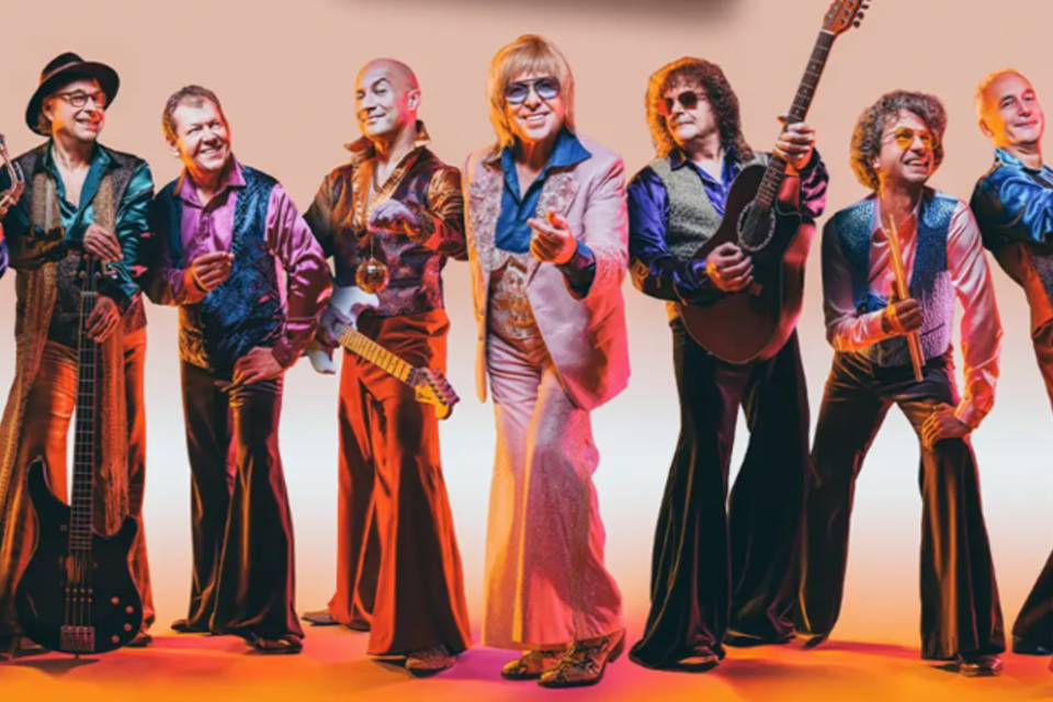 Eine Gruppe von neun Musikern in bunten, vintage Outfits steht zusammen. Sie halten verschiedene Musikinstrumente und lächeln in die Kamera. | © Oststeiermark Tourismus