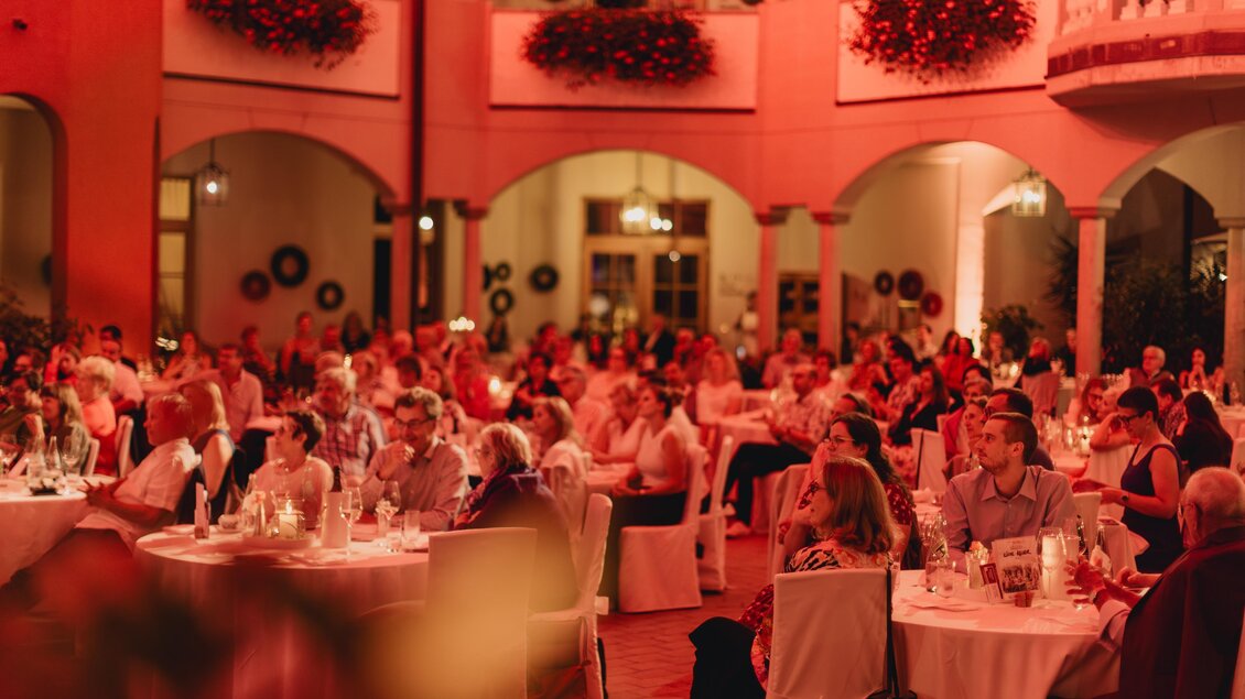 Eine festliche Veranstaltung mit vielen Gästen in einem eleganten Raum. Die Atmosphäre ist warm und einladend, mit rotem Licht und schön gedeckten Tischen. | © Karl Schrotter