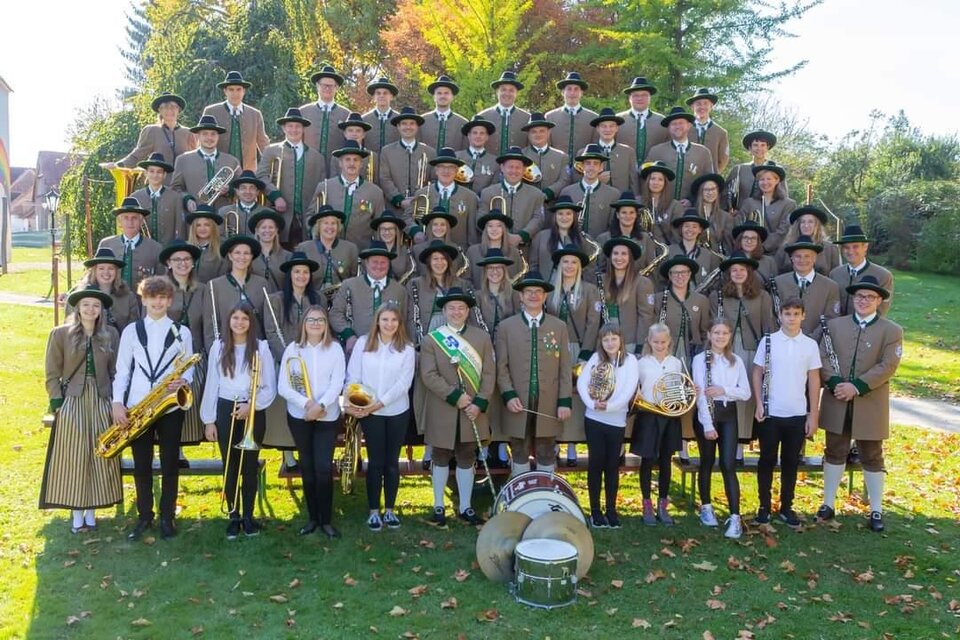 Eine große Gruppe von Menschen in traditionellen Trachten steht im Freien. Sie halten Musikinstrumente und lächeln in die Kamera. | © MMK Bad Waltersdorf