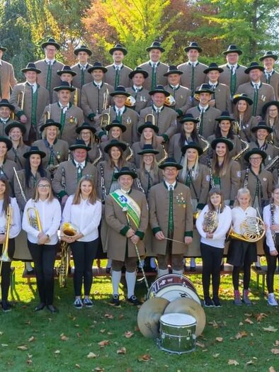 A large group of people in traditional costumes stands outdoors. They are holding musical instruments and smiling at the camera. | © MMK Bad Waltersdorf