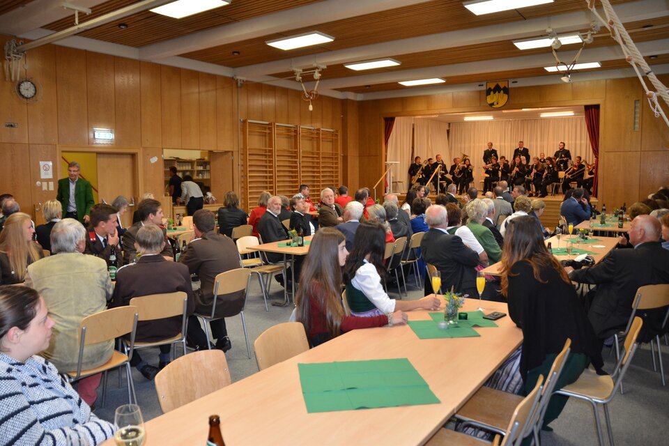 Eine Gesellschaft in einem großen Raum mit Tischen und Stühlen. Im Hintergrund spielt eine Band auf einer Bühne. | © Peter Fritz