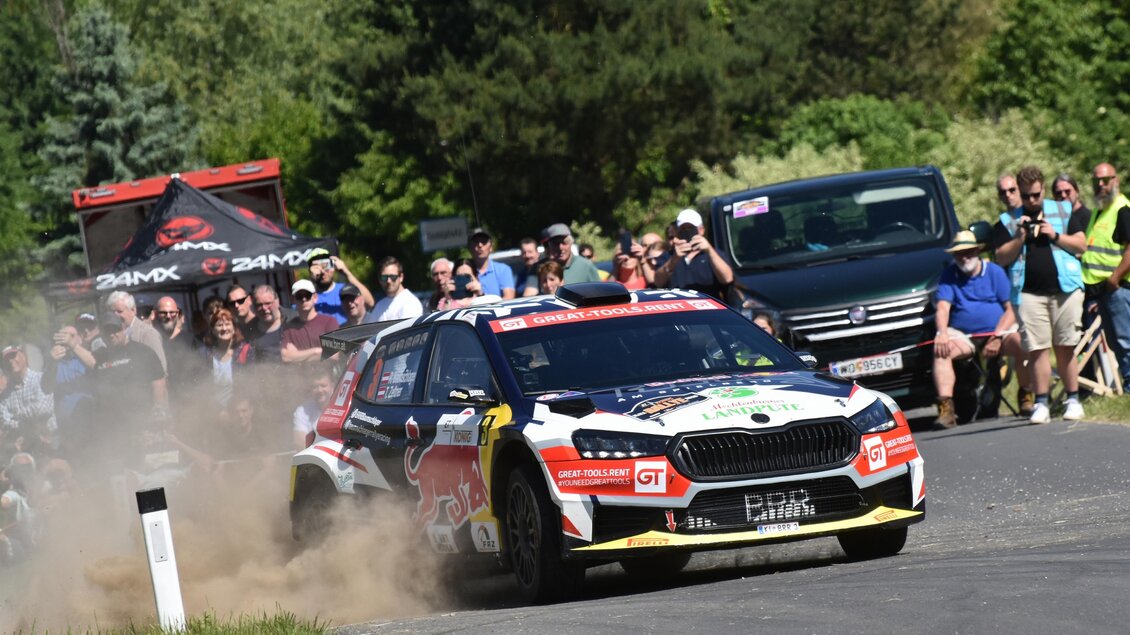 Ein Rennwagen fährt dynamisch auf einer kurvenreichen Straße, umgeben von Zuschauern. Staub wirbelt auf, während das Auto sich schnell bewegt. | © Peter Hopf