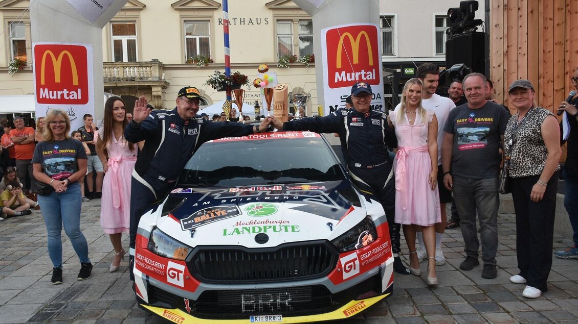 Ein Siegermoment bei einem Motorsport-Event mit einem Rennwagen und mehreren Menschen. Im Hintergrund ist das Stadtbild zu sehen. | © Peter Hopf