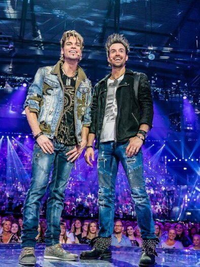 Two musicians stand on a stage with colorful lights and an enthusiastic audience. The atmosphere is festive and energetic. | © ralph-larmann-gross