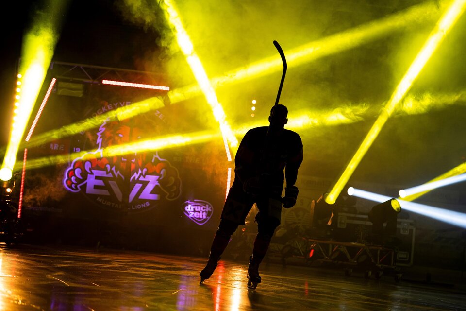 Ein Eishockeyspieler in Silhouette steht auf dem Eis, umgeben von bunten Lichtern. Die Atmosphäre ist dynamisch und energiegeladen. | © EVZ Murtal Lions