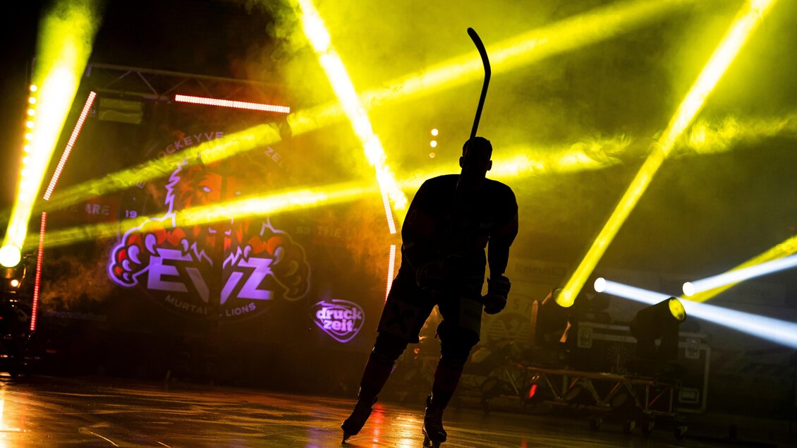 Ein Eishockeyspieler in Silhouette steht auf dem Eis, umgeben von bunten Lichtern. Die Atmosphäre ist dynamisch und energiegeladen. | © EVZ Murtal Lions