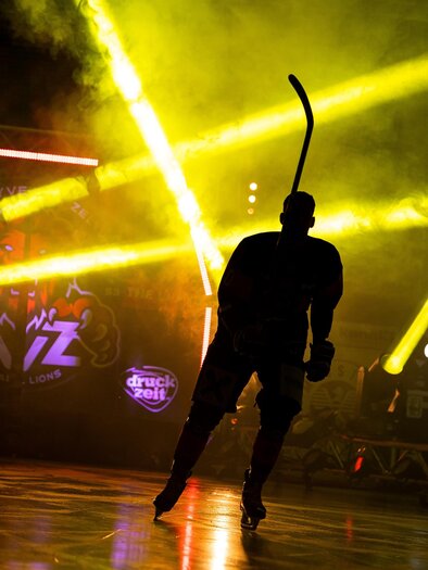 A hockey player in silhouette stands on the ice, surrounded by colorful lights. The atmosphere is dynamic and energetic. | © EVZ Murtal Lions