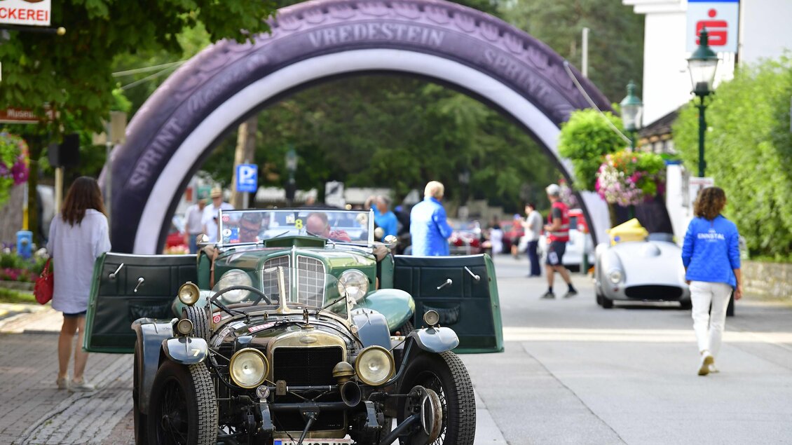 Ein klassisches Auto steht auf einer Straße vor einem大ónicos Bogen. Menschen bewegen sich im Hintergrund, während die Veranstaltung im Gange ist. | © Peter Maierhofer