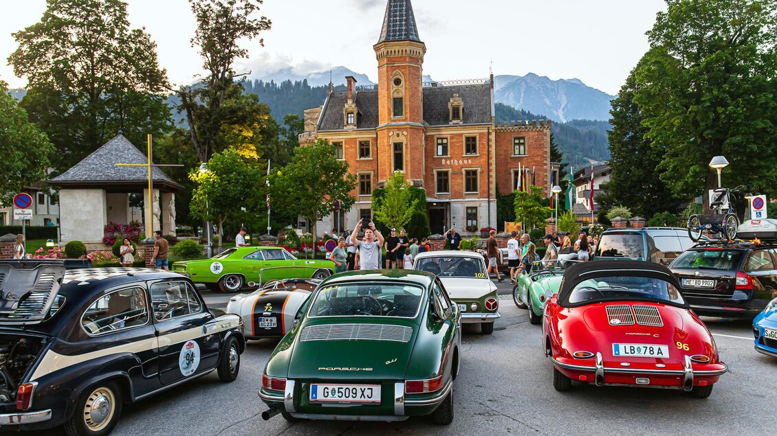 Eine belebte Stadtstraße mit klassischen Autos und einem historischen Gebäude im Hintergrund. Umgeben von grünen Bäumen und Bergen zieht die Szene Aufmerksamkeit an. | © Steering Media