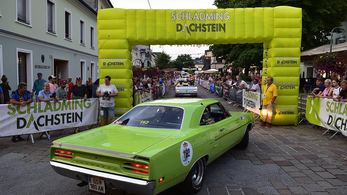 Ein grünes Auto fährt durch ein festliches Tor in der Stadt. Viele Zuschauer stehen an der Straße und beobachten das Ereignis. | © Peter Meierhofer