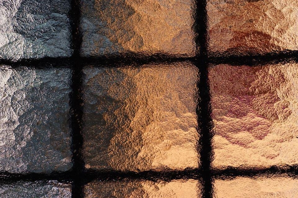 Ein detailreiches Glasfenster mit einem Muster aus schimmernden, glänzenden Oberflächen. Die Farben variieren von Silber bis Gold und schaffen ein interessantes Lichtspiel. | © Vierglaskultur