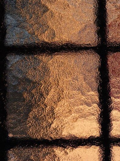 A detailed stained glass window with a pattern of shimmering, glossy surfaces. The colors range from silver to gold, creating an intriguing play of light. | © Vierglaskultur