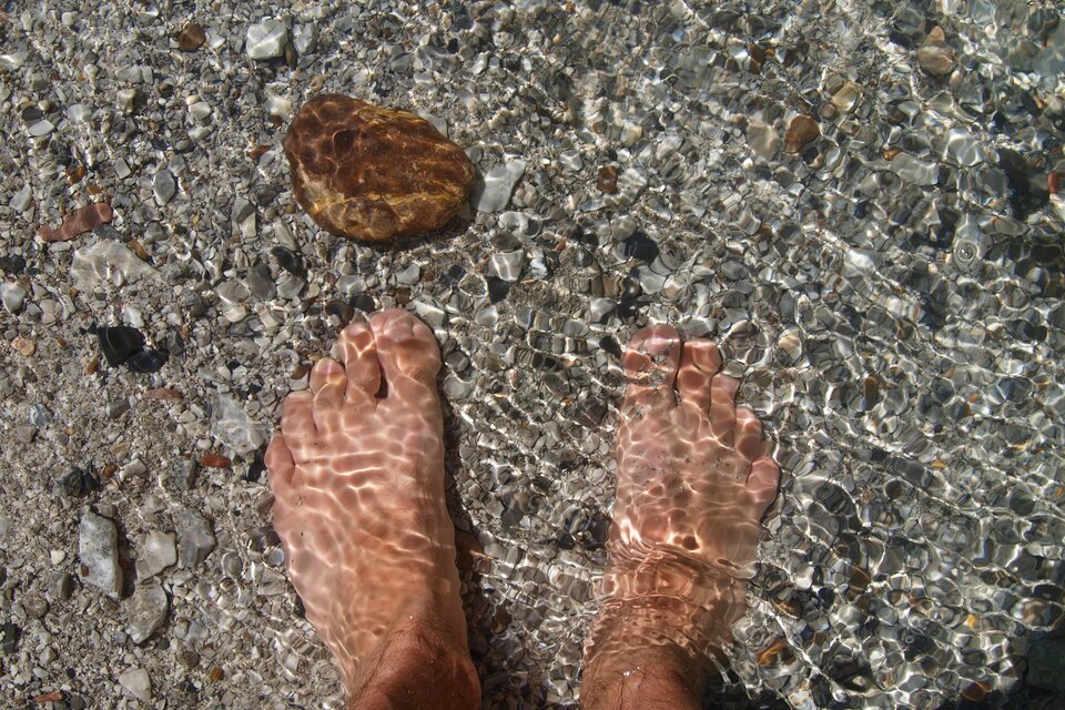 Zwei Füße stehen im klaren Wasser. Im Hintergrund ist ein Stein zu sehen. | © Pixabay