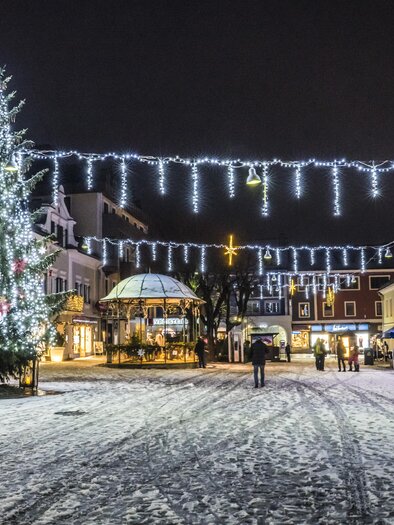 A festively illuminated Christmas market at night. Christmas tree and beautiful lights adorn the snow-covered street. | © Gerhard Pilz
