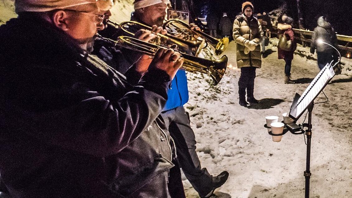 Zwei Musiker spielen Trompete in einem verschneiten Nachtumfeld. Im Hintergrund sind weitere Personen zu sehen, die sich auf einem schmalen Weg bewegen. | © Tourismusverband Schladming-Dachstein