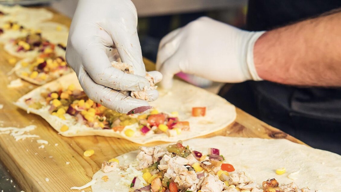 Ein Koch bereitet frische Wraps mit Hähnchen, Gemüse und anderen Zutaten vor. Die Zubereitung findet auf einer Holzplatte statt. | © European Street Food Festival
