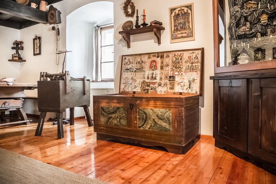 Ein gemütlicher Raum mit rustikaler Einrichtung. Im Vordergrund steht eine verzierte Holztruhe und im Hintergrund sind weitere Möbel und Dekorationen zu sehen. | © TV Hochsteiermark, Fred Lindmoser