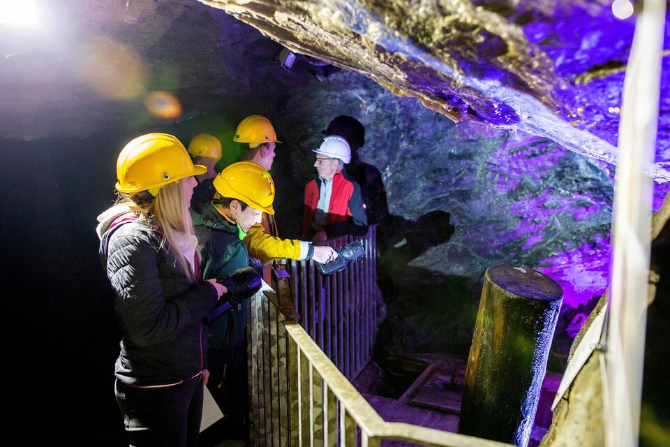 Eine Gruppe von Personen trägt Helme und erkundet eine Höhle. Sie schauen sich einen beleuchteten Bereich mit interessanten Felsformationen an. | © K. Painer