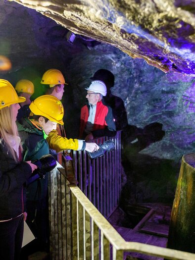 Eine Gruppe von Personen trägt Helme und erkundet eine Höhle. Sie schauen sich einen beleuchteten Bereich mit interessanten Felsformationen an. | © K. Painer