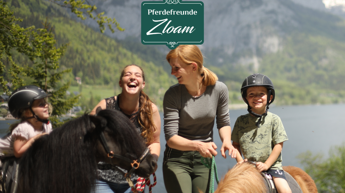 Eine fröhliche Gruppe von Menschen lacht und reitet auf Ponys in einer landschaftlich schönen Umgebung. Im Hintergrund sind Berge und ein See zu sehen. | © Narzissendorf Zloam, www.zloam.at