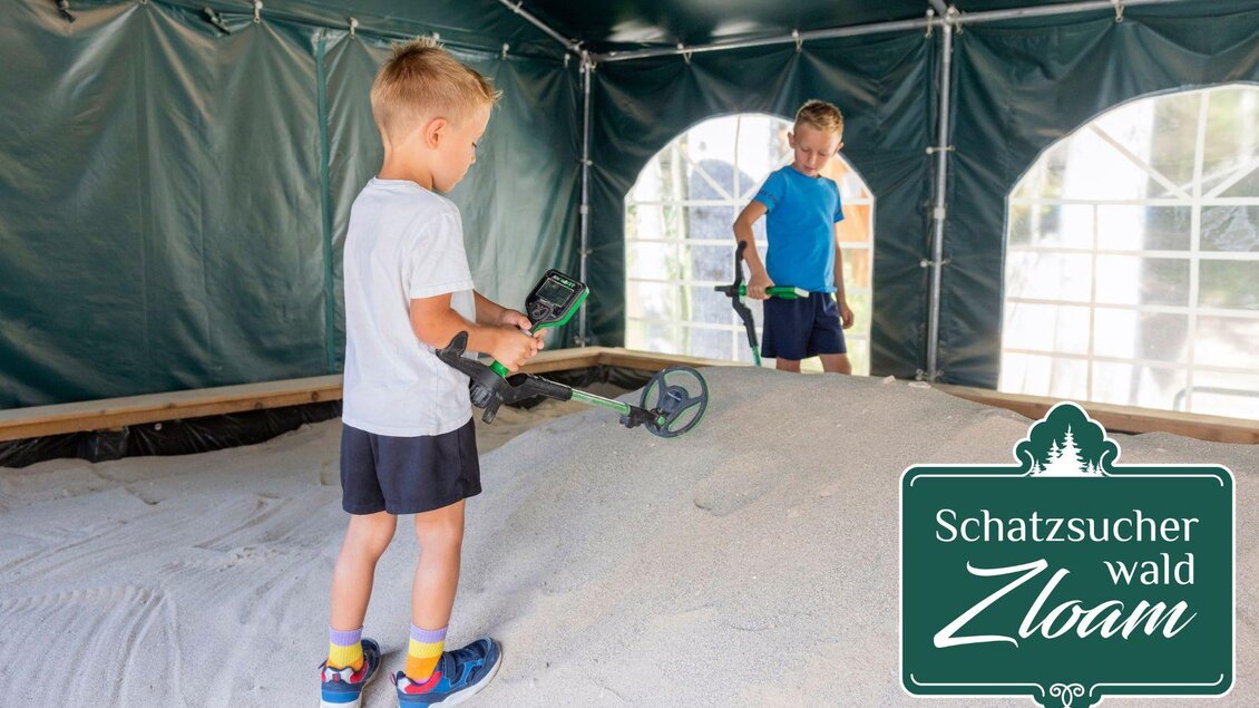 Zwei Kinder stehen in einem Zelt und suchen mit Metalldetektoren im Sand nach Schätzen. Der Raum ist gut beleuchtet und freundlich gestaltet. | © www.zloam.at