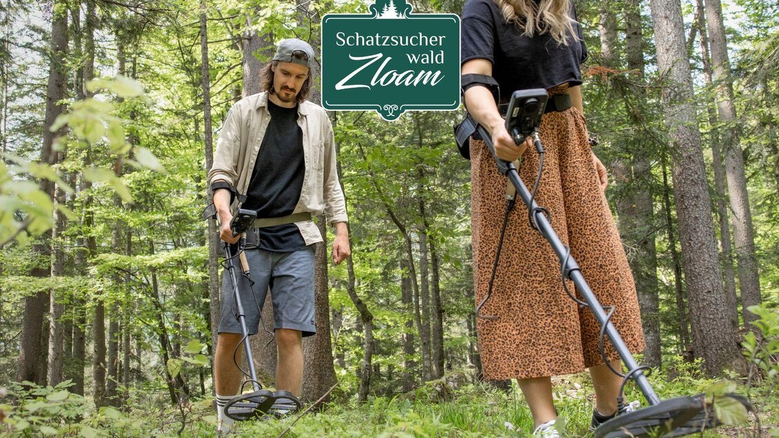 Zwei Personen suchen mit einem Metalldetektor im Wald nach Schätzen. Die Umgebung ist grün und bewaldet, ideal für Entdeckungen. | © Narzissendorf Zloam, www.zloam.at