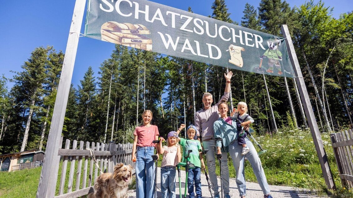 Eine Gruppe von Menschen steht vor einem Schilder mit der Aufschrift "Schatzsucher Wald". Im Hintergrund sind Bäume und eine blühende Landschaft zu sehen. | © www.zloam.at
