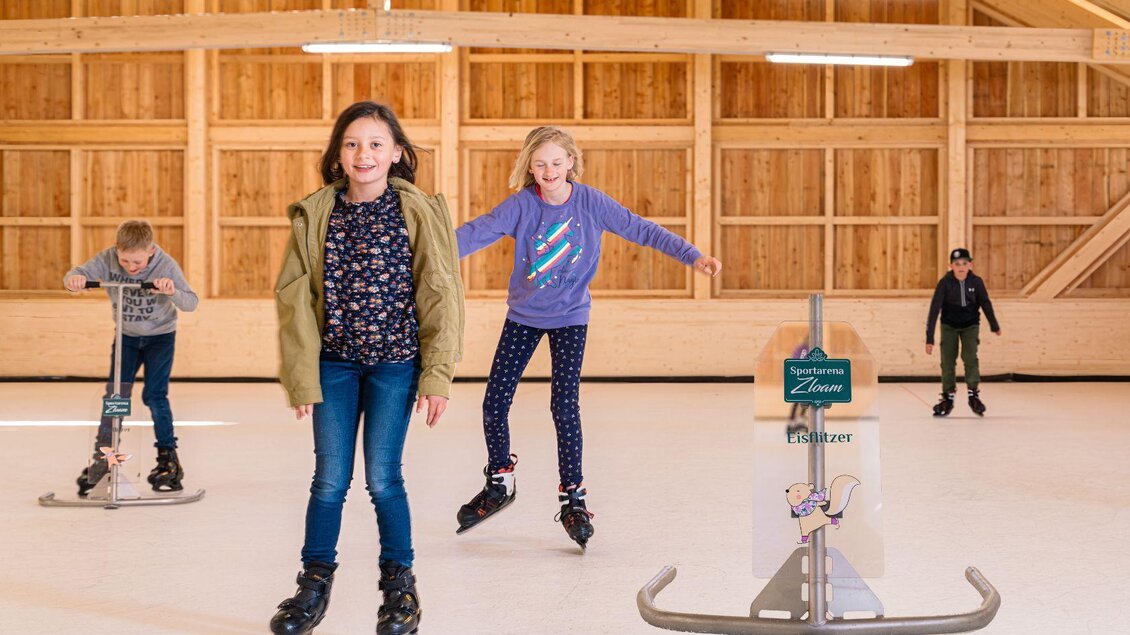 Eine Gruppe von Kindern auf einer Eislauffläche. Zwei Kinder üben das Eiskunstlaufen, während die anderen im Hintergrund Spaß haben. | © www.zloam.at