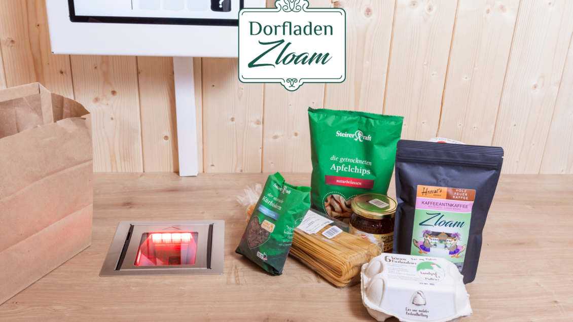 Ein gemütlicher Marktbereich mit Lebensmitteln und einer digitalen Kasse. Verschiedene Produkte wie Nudeln, Eier und Snacks sind auf einem Holztisch angeordnet. | © Narzissendorf Zloam, www.zloam.at