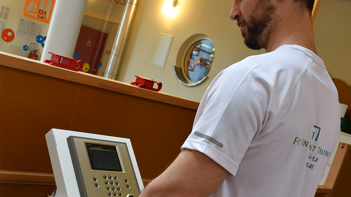 Ein Mann testet ein Fitnessgerät in einem modernen Trainingsraum. Im Hintergrund sind verschiedene Geräte und symbolische Fitness-Elemente sichtbar. | © H2O-Hoteltherme GmbH / FIT