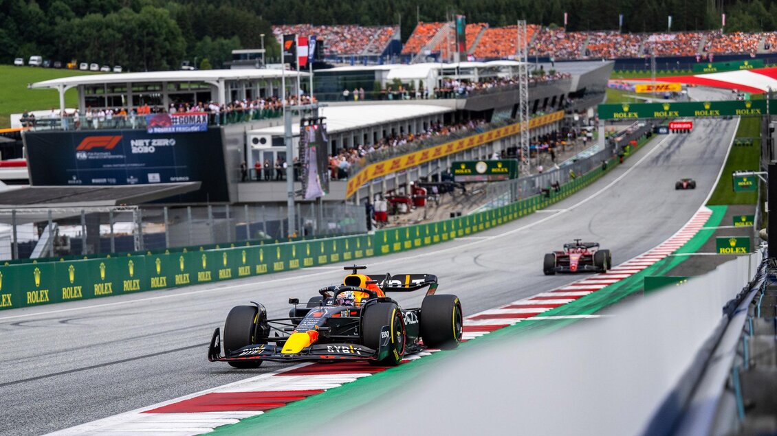 Ein Formel-1-Rennwagen fährt auf der Rennstrecke, umgeben von einer lebhaften Zuschauermenge. Im Hintergrund sind die pit lane und die Berge zu sehen. | © Joerg Mitter Red Bull Ring