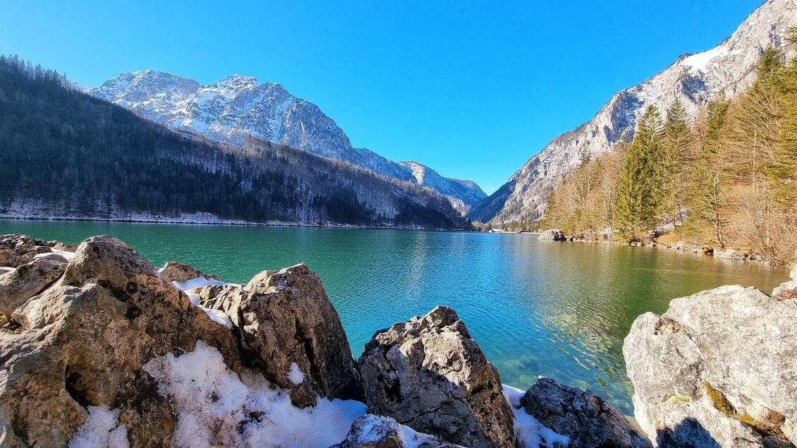 Eine malerische Berglandschaft mit einem klaren, türkisfarbenen See. Umgeben von schneebedeckten Bergen und Nadelbäumen. | © Hirtler
