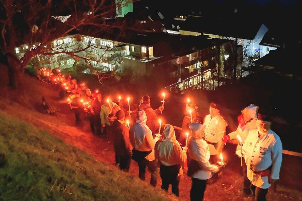 Eine Gruppe von Menschen steht in einer Reihe und hält Fackeln in der Nacht. Im Hintergrund sind beleuchtete Gebäude sichtbar. | © Schaubergwerk Oberzeiring